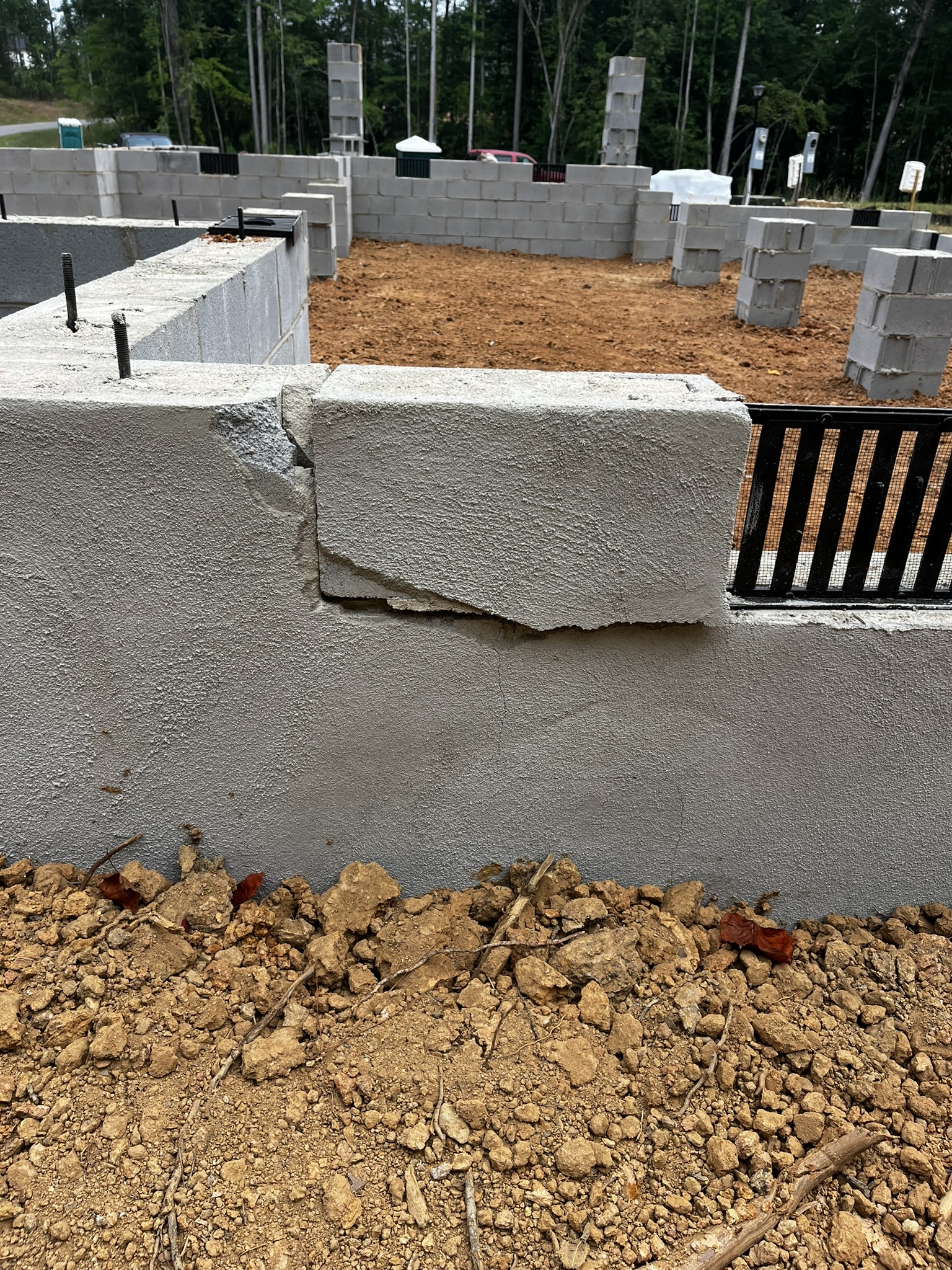 Chipped corner foundation block next to a black louvered crawlspace vent