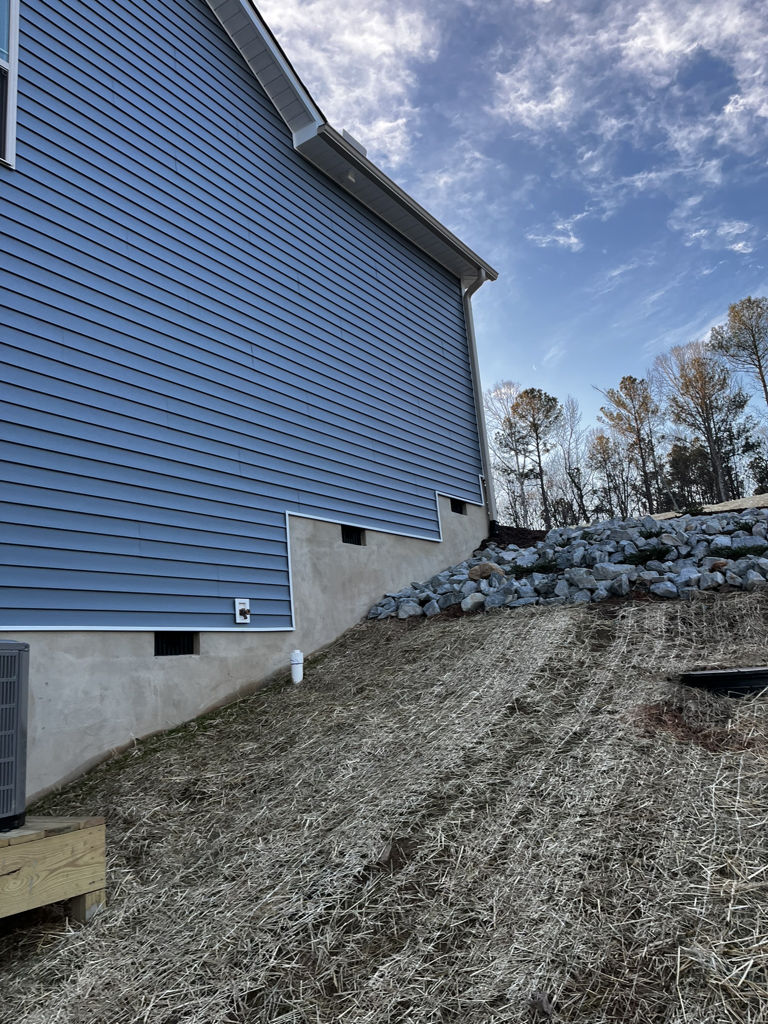 Side of home showing masonry foundation transitioning up a steep graded slope